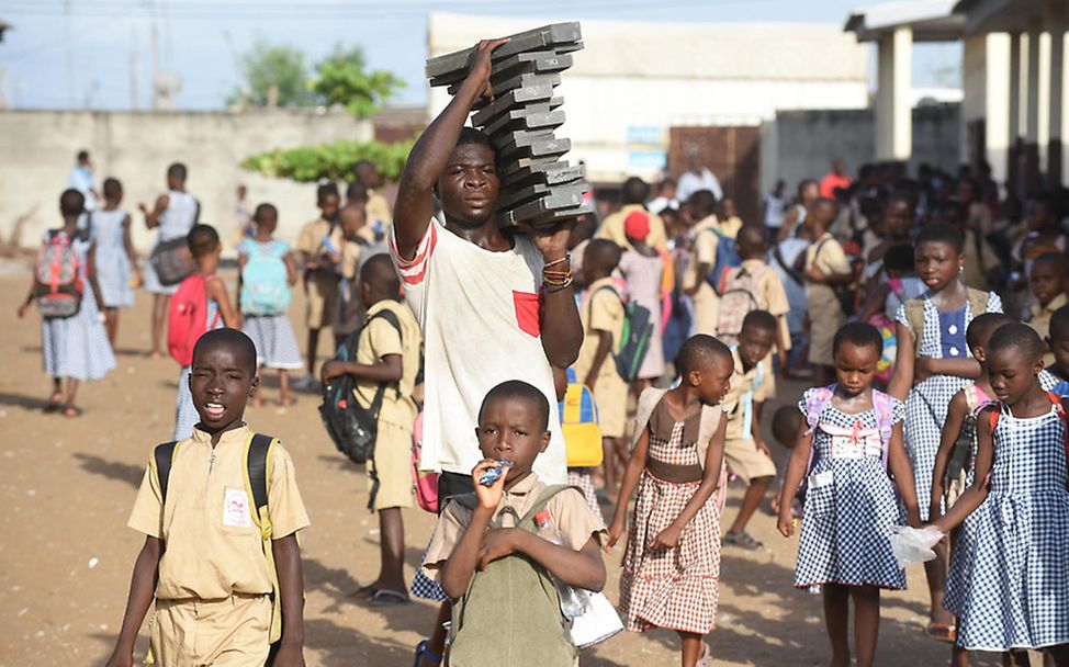 Abidjan: Schulkinder und ein Mann, der die Bausteine für den Bau der Schule trägt