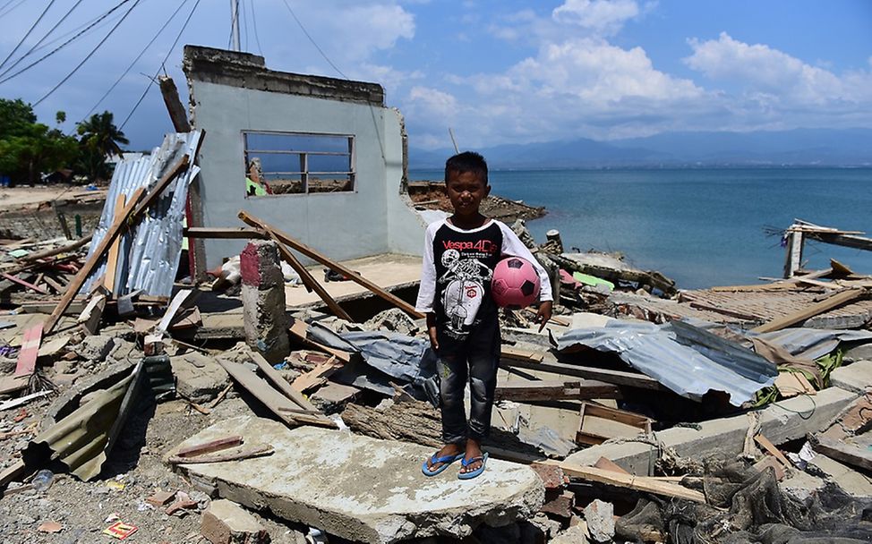 Ein Junge steht vor einem zerstörten Haus