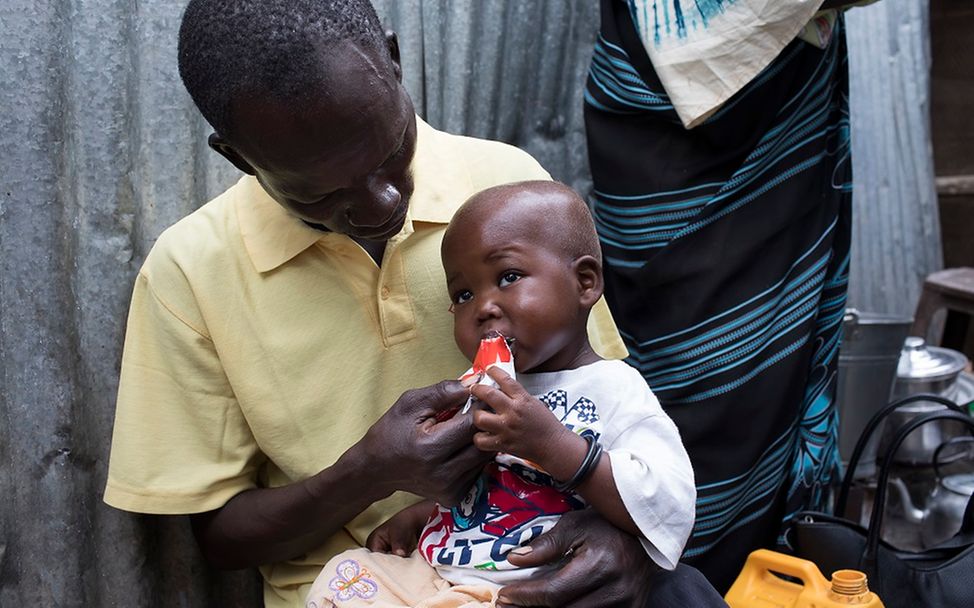 Ein Vater füttert sein Kind mit Erdnusspaste.