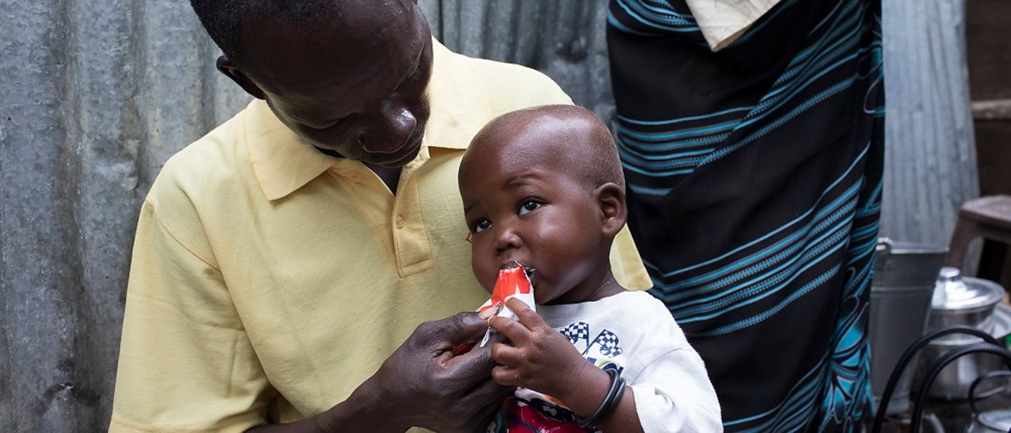 Ein Vater füttert sein Kind mit Erdnusspaste.