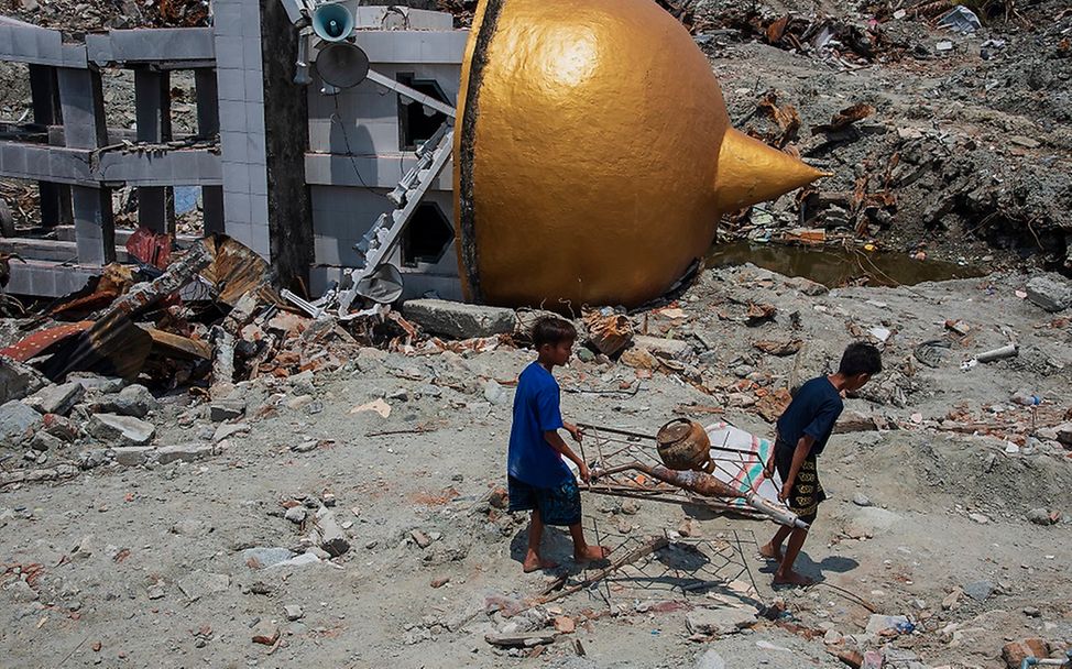 Zwei Jungen transportieren Metal zum Verkauf durch eine von Zerstörung gekennzeichnete Umgebung.