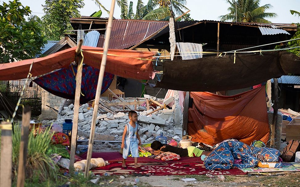 Junge vor den Trümmern eines Hauses in Indonesien
