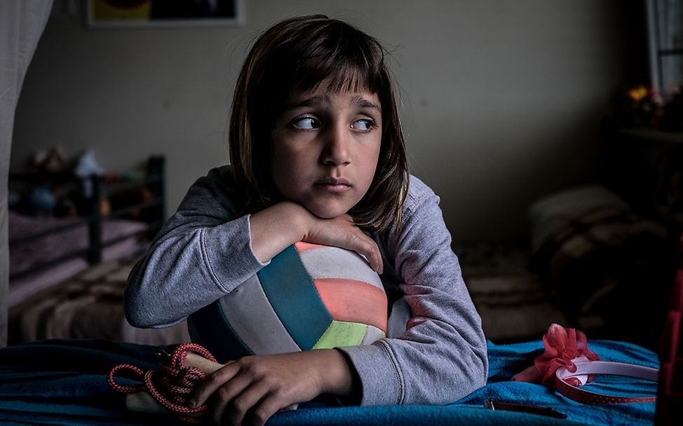 Ein Mädchen in einer Flüchtlingsunterkunft lehnt sich traurig über einen Ball.
