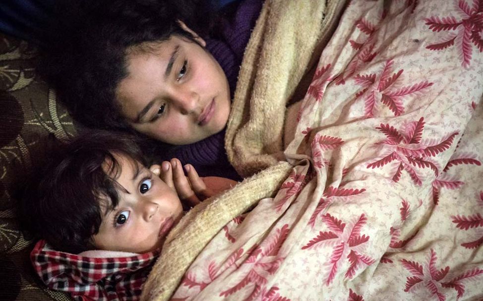 Winterhilfe Syrien: Zwei geflüchtete syrische Geschwister schützen sich unter einer Decke vor der Kälte. 