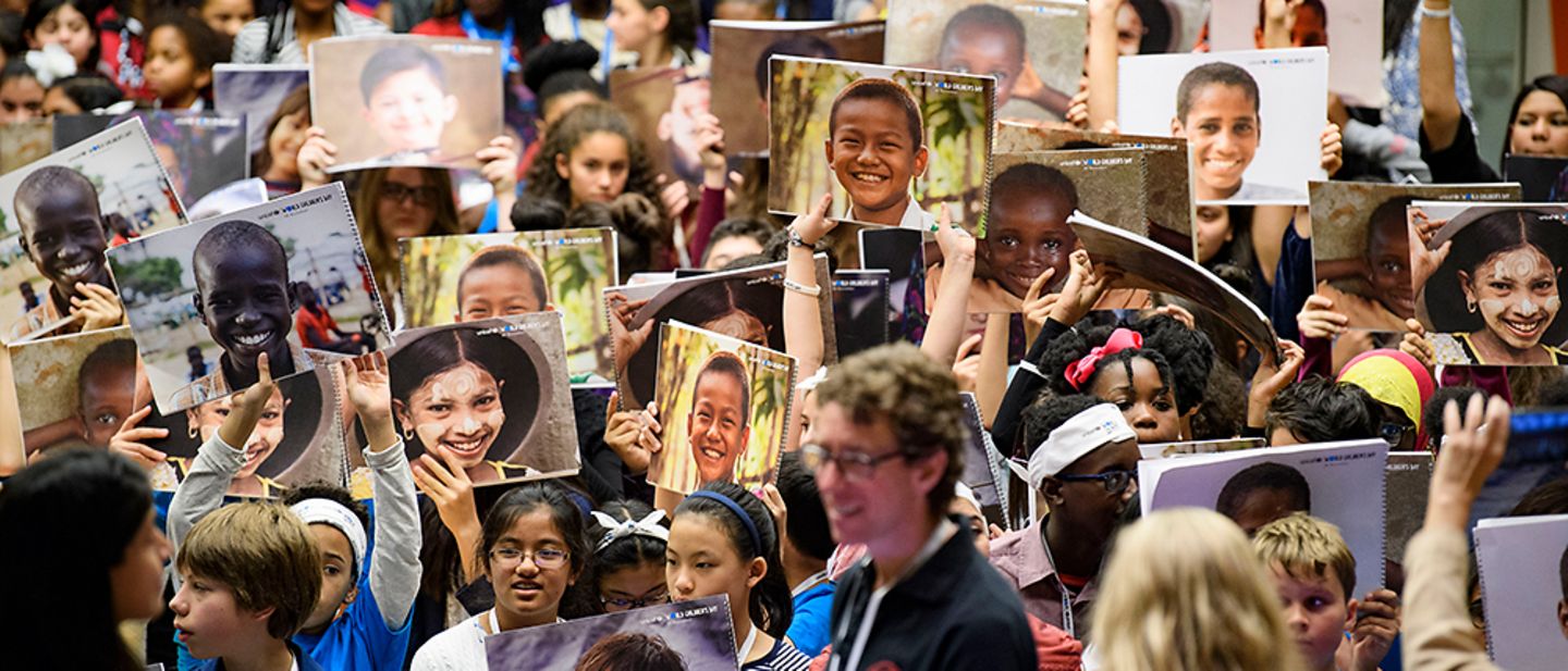 UN-Kinderrechtskonvention: Teilnehmer des Weltkindertages halten Bilder mit lachenden Kindern hoch.