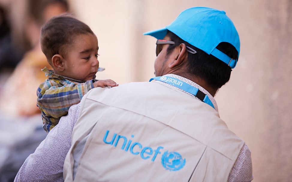 Syrien: Ein UNICEF-Mitarbeiter trägt einen Jungen
