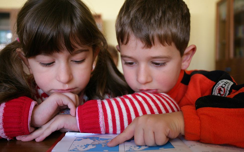 Albanien: Zwei Kinder gucken sich eine Karte in einem Buch an