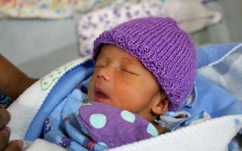 Ein frühgeborenes Baby mit einem Wollmützchen auf dem Kopf. 