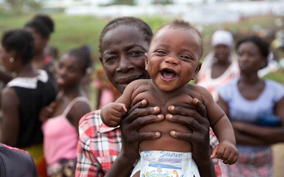 Mosambik: Eine Frau hält ihr lachendes Baby hoch.