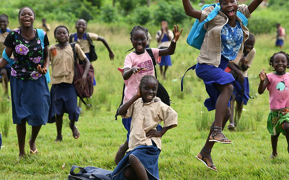 Kongo: Schulmädchen springen fröhlich über eine Wiese.