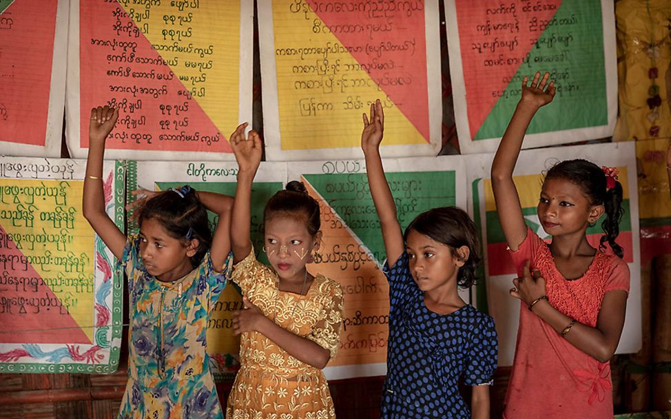 Bangladesch: Vier Mädchen melden sich vor einer Plakatwand einer Notschule.