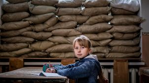 Ostukraine: Die 10-jährige Lera sitzt vor den durch Sandsäcke bedeckten Fenstern.