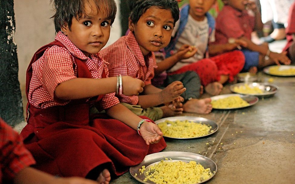 Kinder sitzen in einer Reihe und essen Reis von ihren Tellern. 