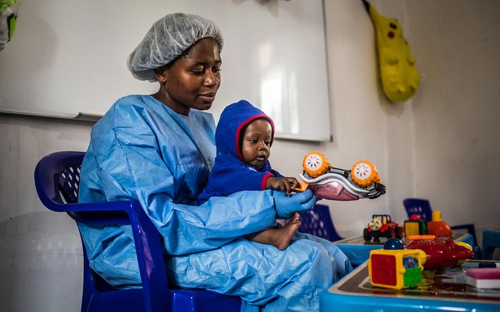 Eine Ebola-Überlebende in Ebola-Schutzkleidung spielt mit einem Baby.