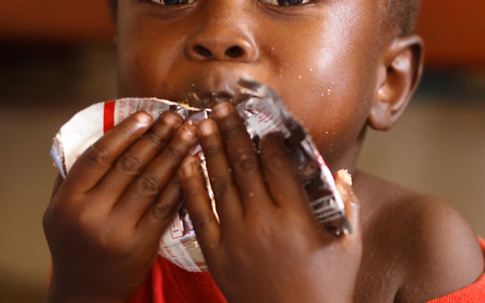 Ghana: Ein Junge isst genüsslich ein Päckchen Erdnusspaste.