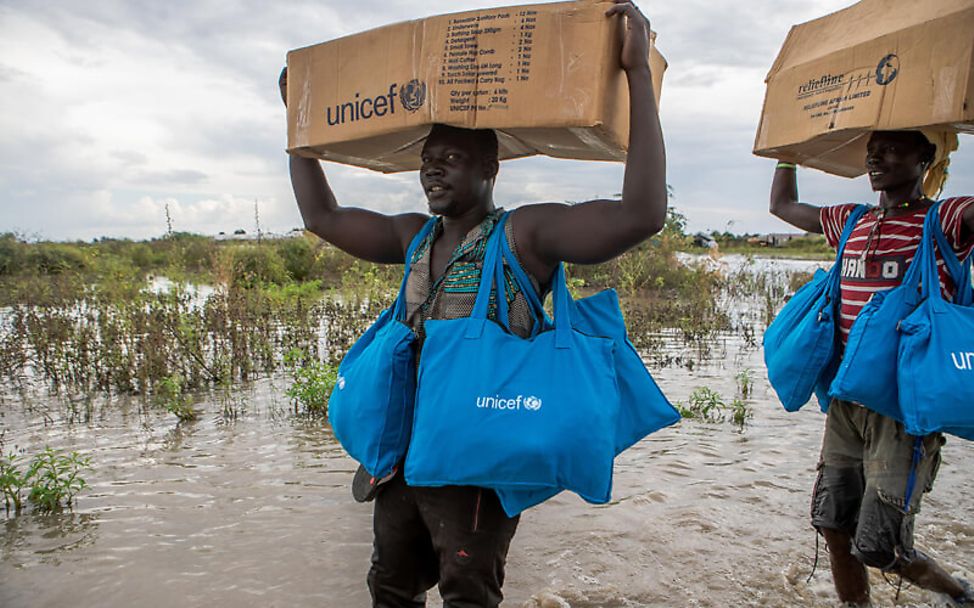 Südsudan: UNICEF-Mitarbeiter tragen Hilfsgüter durch überschwemmte Gebiete
