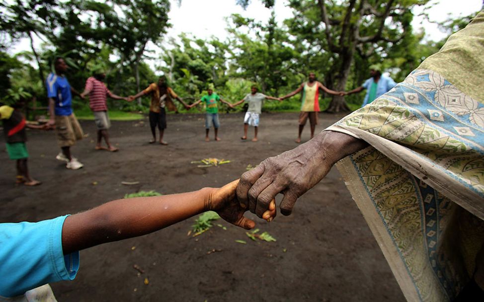 Vanuatu: Dorfbewohner bilden einen Spielkreis und halten sich an den Händen.