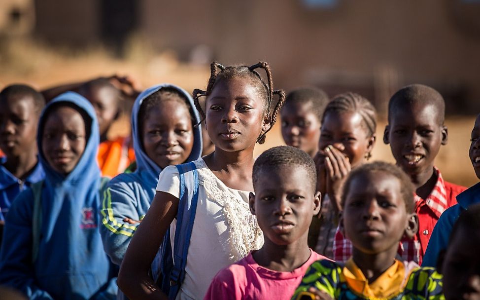 Burkina Faso: Ein Mädchen steht mit ihren Mitschülern in einer Schlange vor dem Schulgebäude.