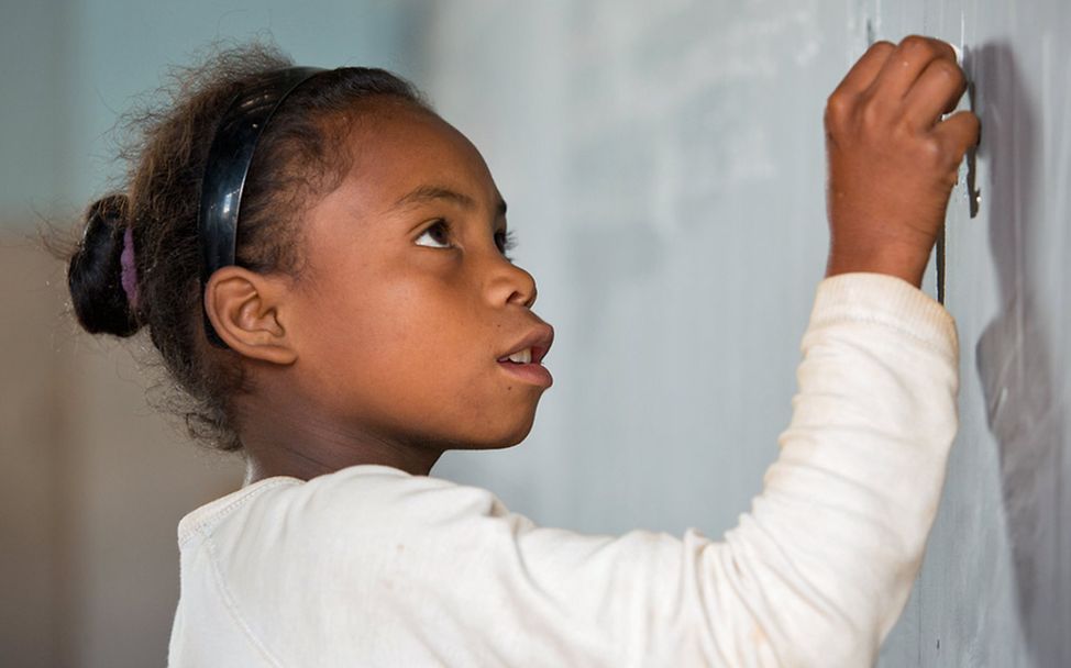Schulen in Afrika: Ein Mädchen in Madagaskar schreibt mit Kreide an eine Tafel. 