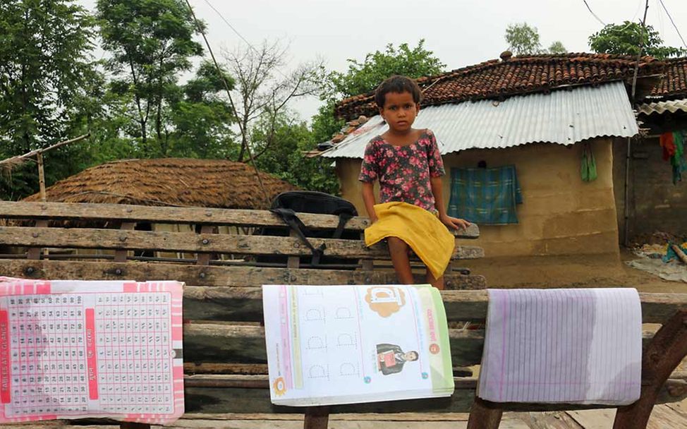 Nepal Naturkatastrophen: Mädchen sitzt auf Bank und trocknet Schulmaterial