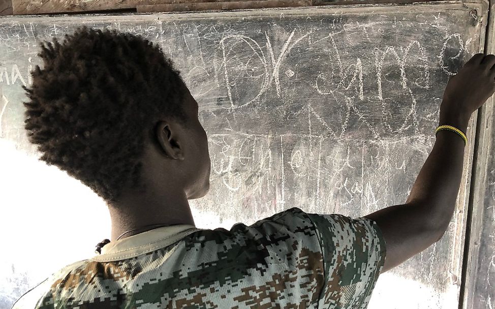 Südsudan 2020: Ein Jugendlicher schreibt mit Kreide an eine Tafel