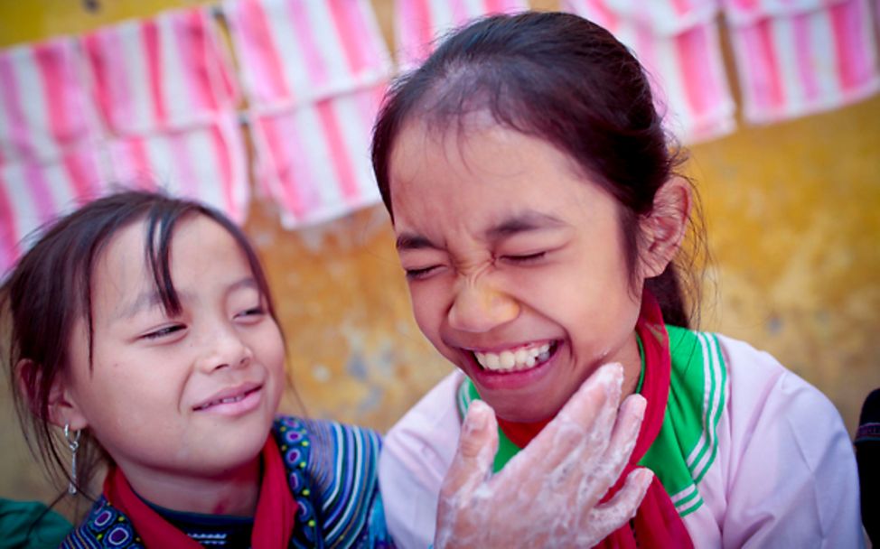 Zwei Schulmädchen waschen ihre Hände mit viel Seife in Vietnam.