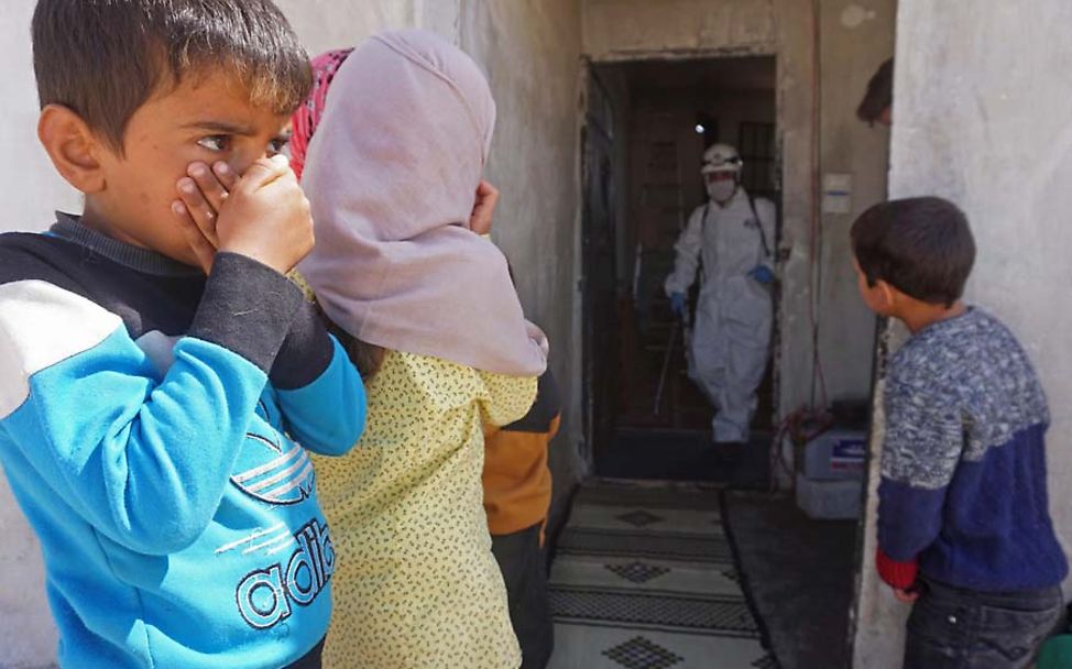 Syrische Kinder beobachten, wie ein Schulgebäude desinfiziert wird.
