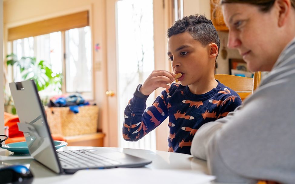 Ein achtjähriger Junge sitzt mit seiner Mutter zuhause vor einem Laptop.
