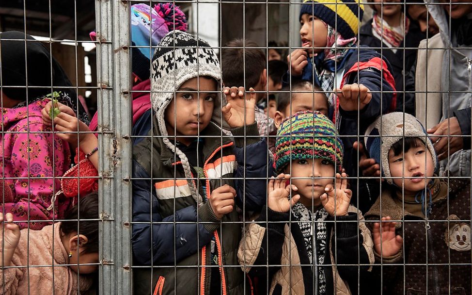 Kinder mit Wollmützen stehen hinter einem Gitter im Flüchtlingslager Moria.