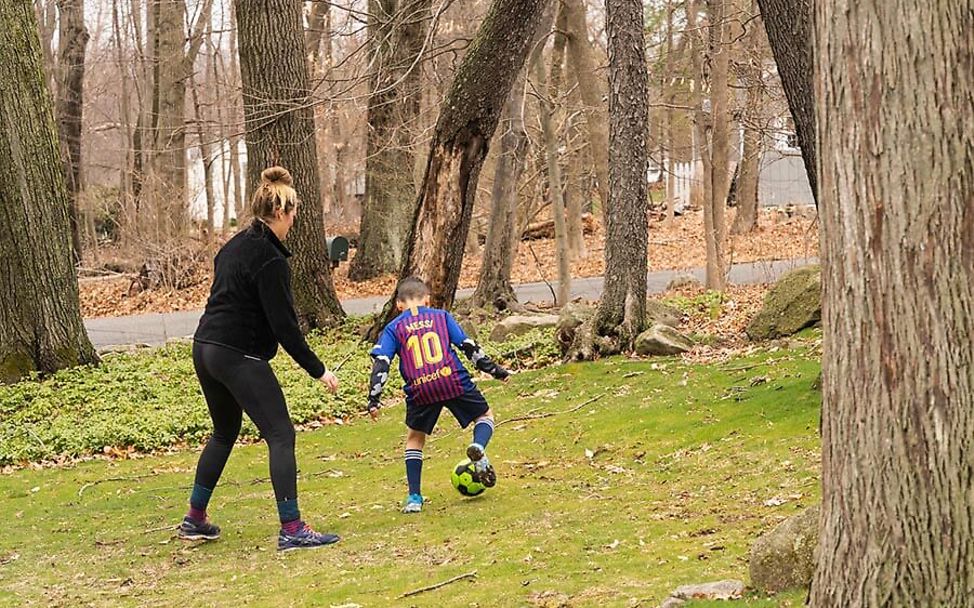 USA: Luka (8) spielt mit seiner Mutter Sophia Fußball in einem Waldstück.