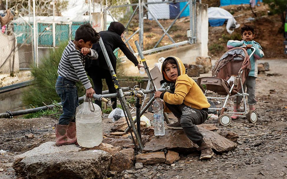 Samos: Zwei Kinder füllen an einem Rohrkonstrukt Wasser in Plastikbehätnisse ab.