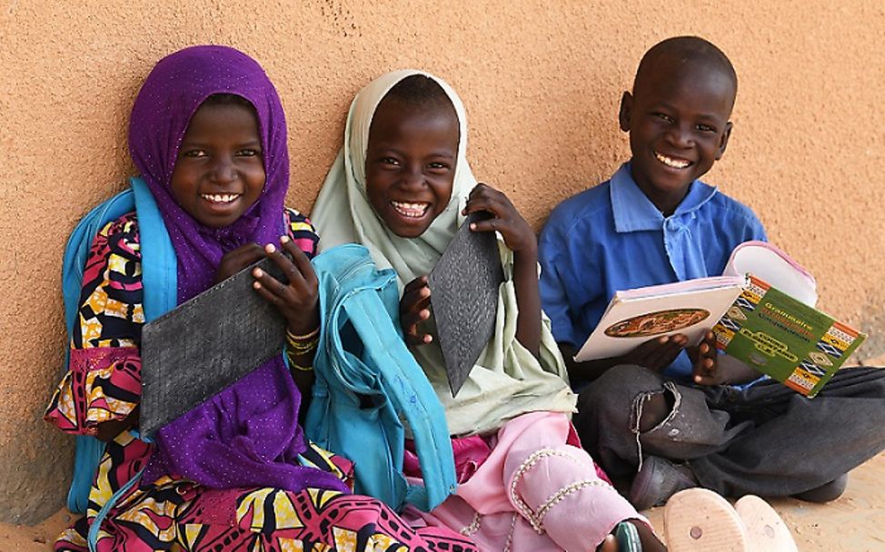 Burkina Faso: Drei Schüler sitzen lächelnd an einer Wand. 