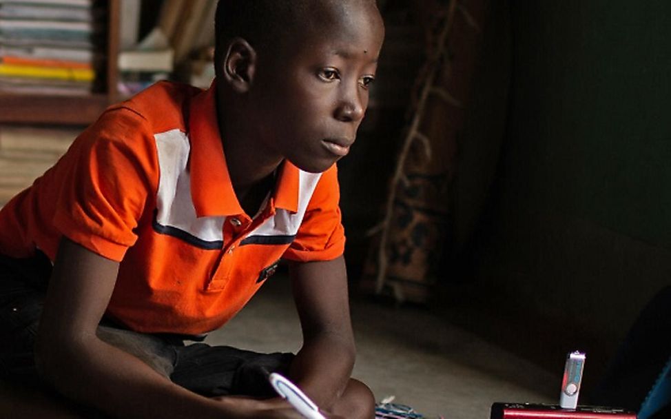 Burkina Faso: Junge sitzt auf dem Boden und lernt per Radio.