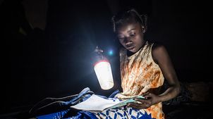 Burkina Faso: Mädchen sitzt im Dunkeln und lernt mit einer Lampe.