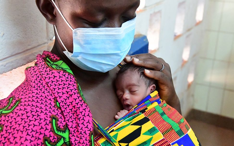 Schwangerschaft während Covid-19: Eine Frau mit Schutzmaske mit einem Neugeborenen auf der Brust