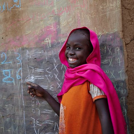 Flüchtlingslager Sudan: Mädchen schreibt mit Kreide an Wand.