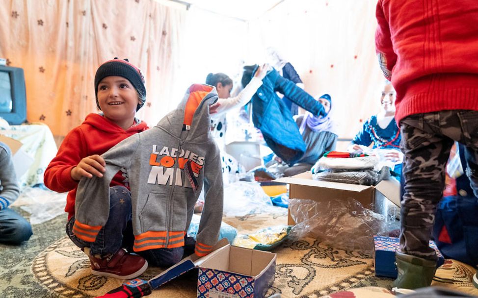 Spenden Syrien: Ein Mädchen packt ein UNICEF-Hilfspaket mit Kleidung aus.