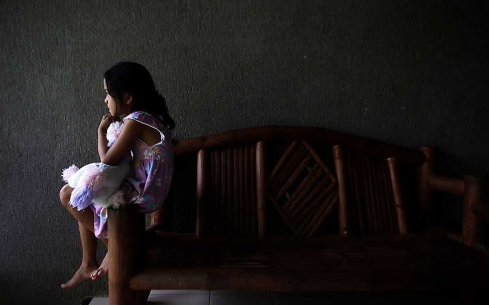 Gewalt gegen Kinder: Mädchen sitzt traurig auf einer Lehne.