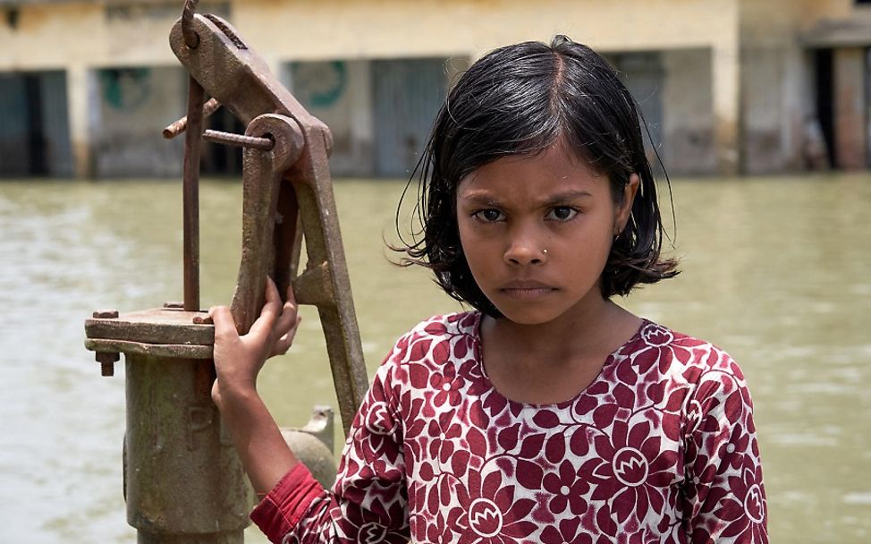 Bangladesh: Ein Mädchen steht neben einer Wasserpumpe.