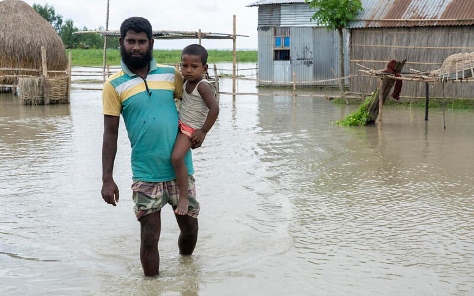 Monsun 2020 in Bangladesch: Ein Vater steht mit seinem Kind auf dem Arm im Hochwasser