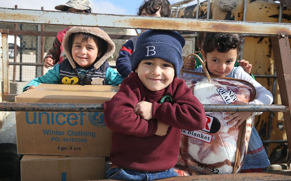 Syrien: Drei Kinder freuen sich über ihre UNICEF-Pakete mit warmer Kleidung.
