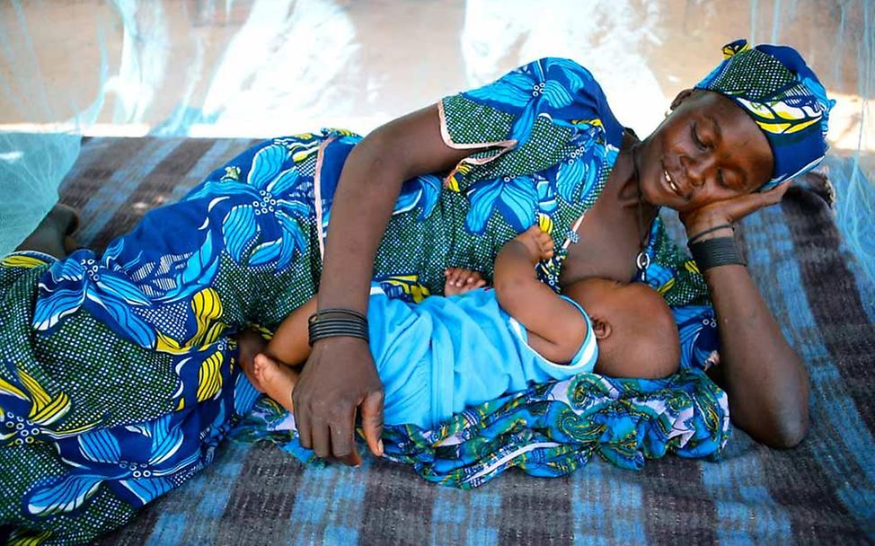 Eine Mutter stillt ihr Kind unter einem Moskitonetz © UNICEF/Pirozzi