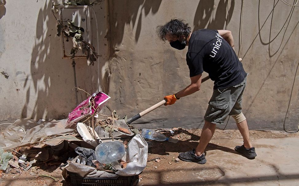 Mann mit UNICEF-Shirt räumt mit einer Schaufel die Trümmer beiseite.