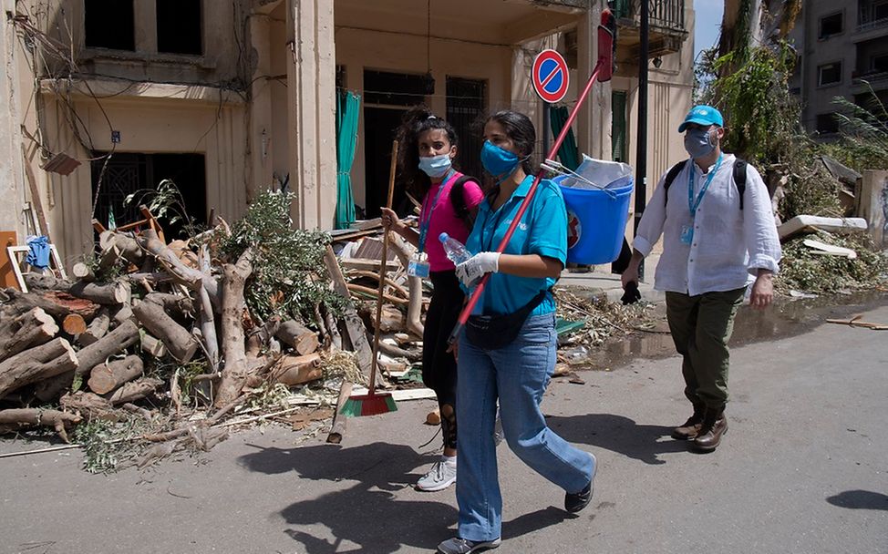 Drei Helfer mit Besen und Eimern laufen durch die verwüsteten Straßen von Beirut.