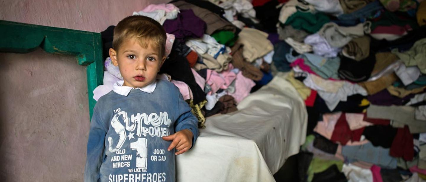 Rumänien: Ein 3-jähriger Junge steht in einem ärmlich eingerichteten Zimmer.