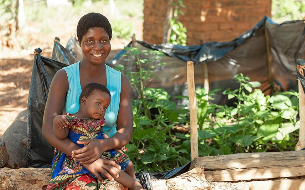 Malawi: Elizabeth sitzt lächelnd mit ihrer Tochter auf der eigenen Gartenmauer.