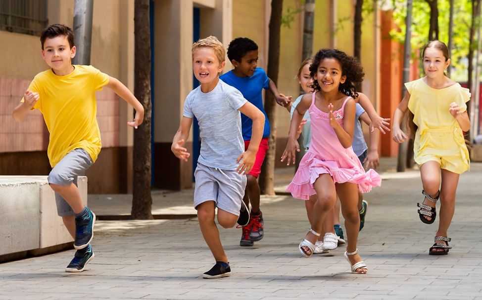 Weltkindertag: Sieben Jungen und Mädchen laufen lachend über die Starße