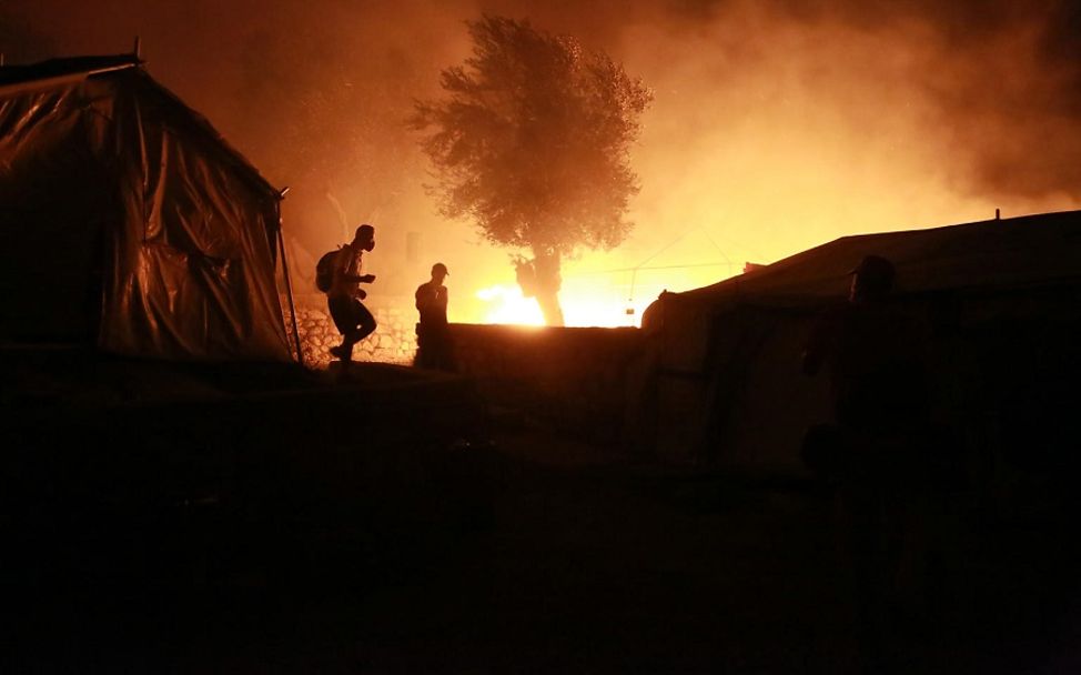 Feuer im Flüchtlingslager Moria: Umrisse von zwei Personen und einem Zelt vor den Flammen