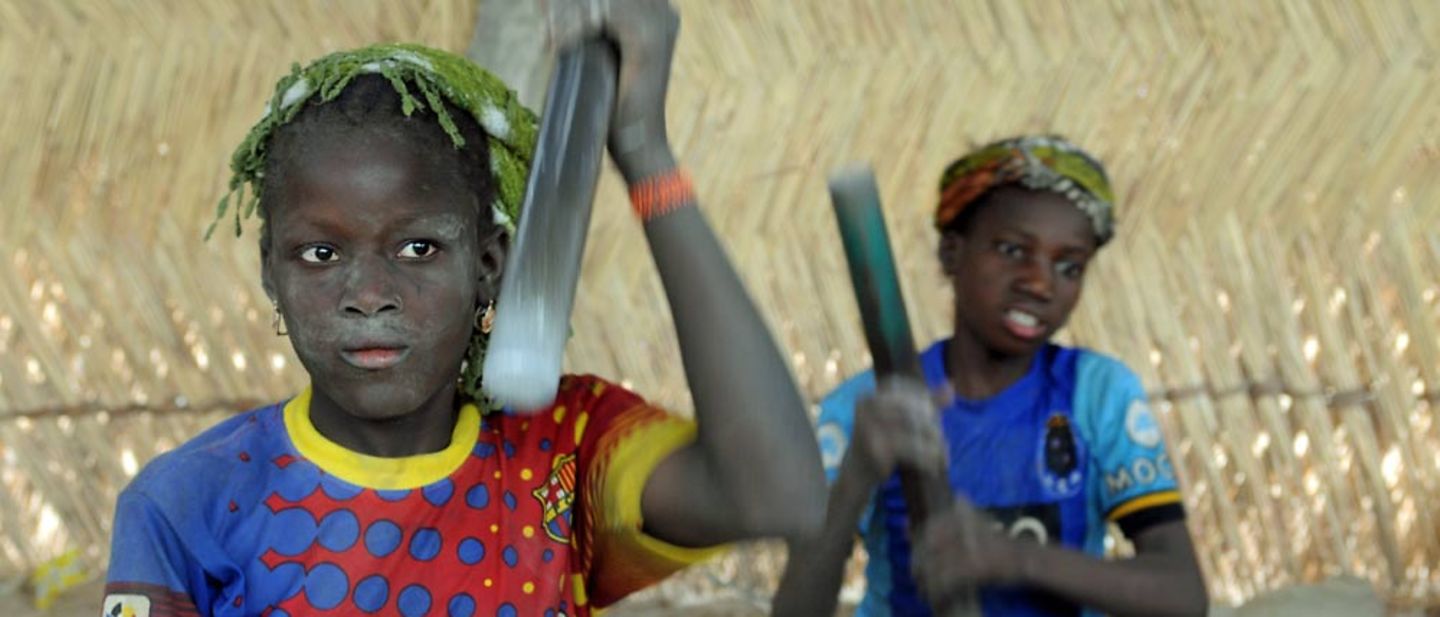 Eine Jugendliche in Burkina Faso klopft in einer Hütte mit einem großen Hammer Steine.