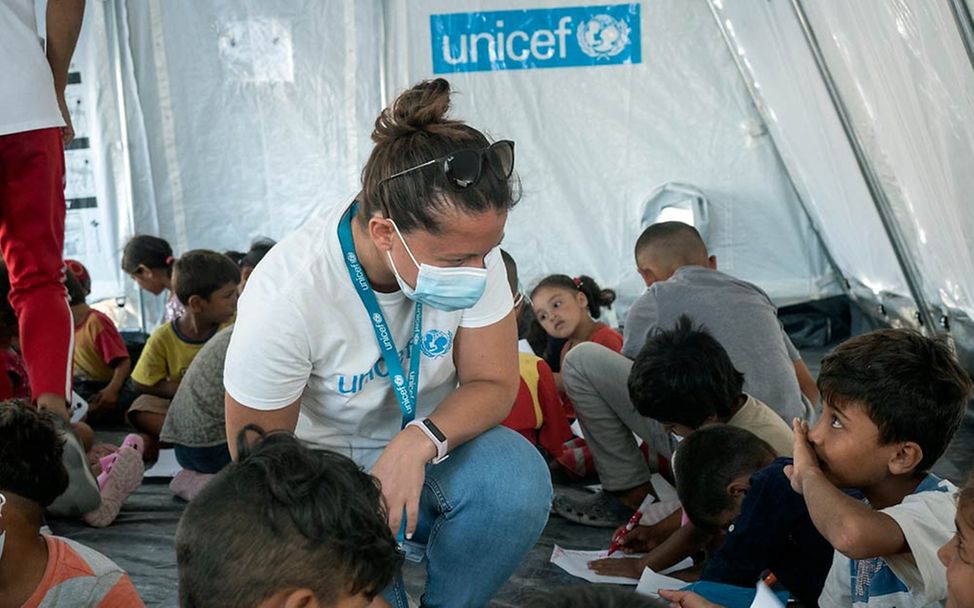 Eine UNICEF-Mitarbeiterin hockt in einem UNICEF-Zelt zwischen malenden Kindern.